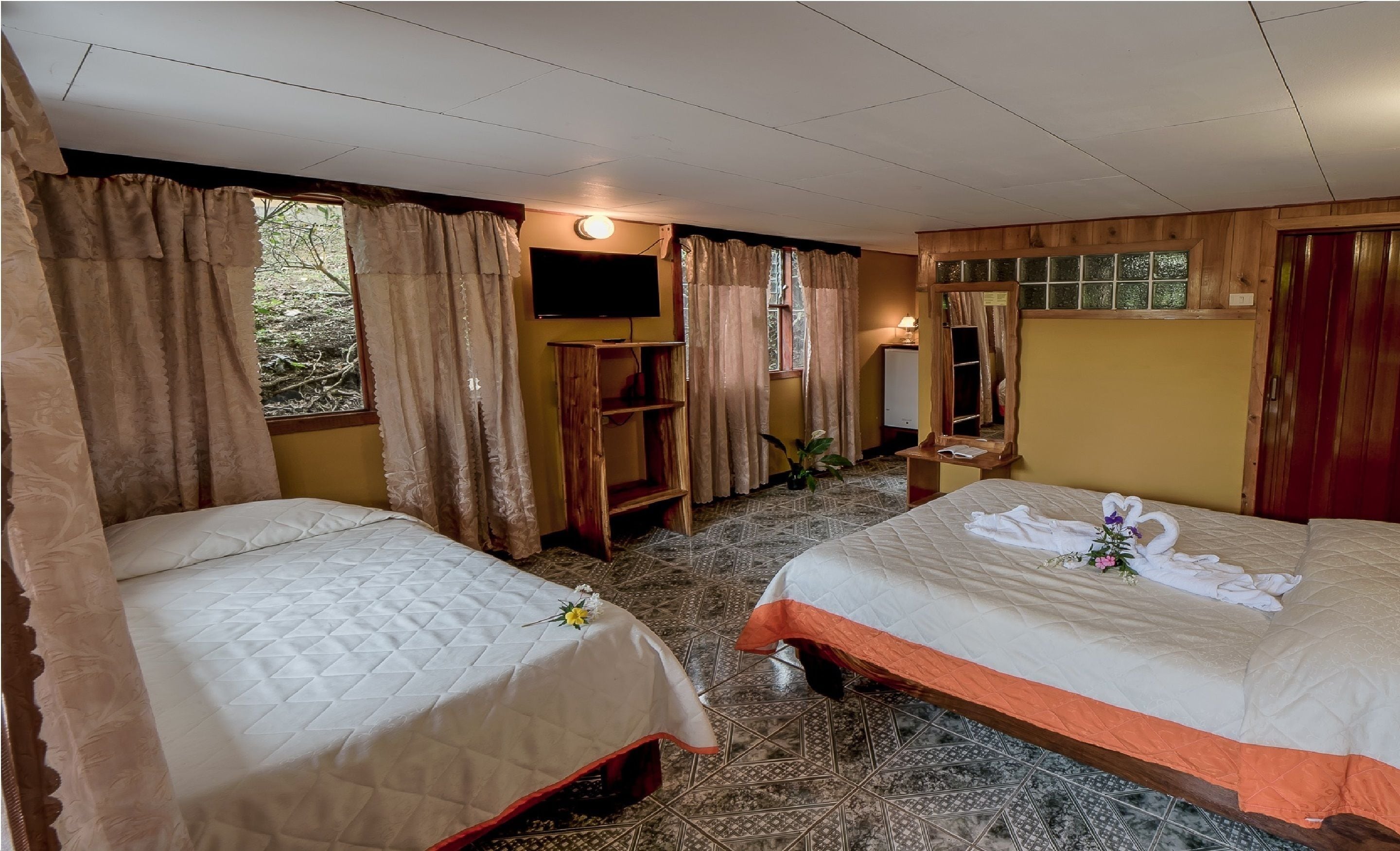 A hotel room with two beds, a TV, a wooden shelf, and a window with curtains.