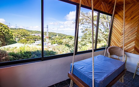 A room with a swing bed, large windows, and a view of a green landscape.