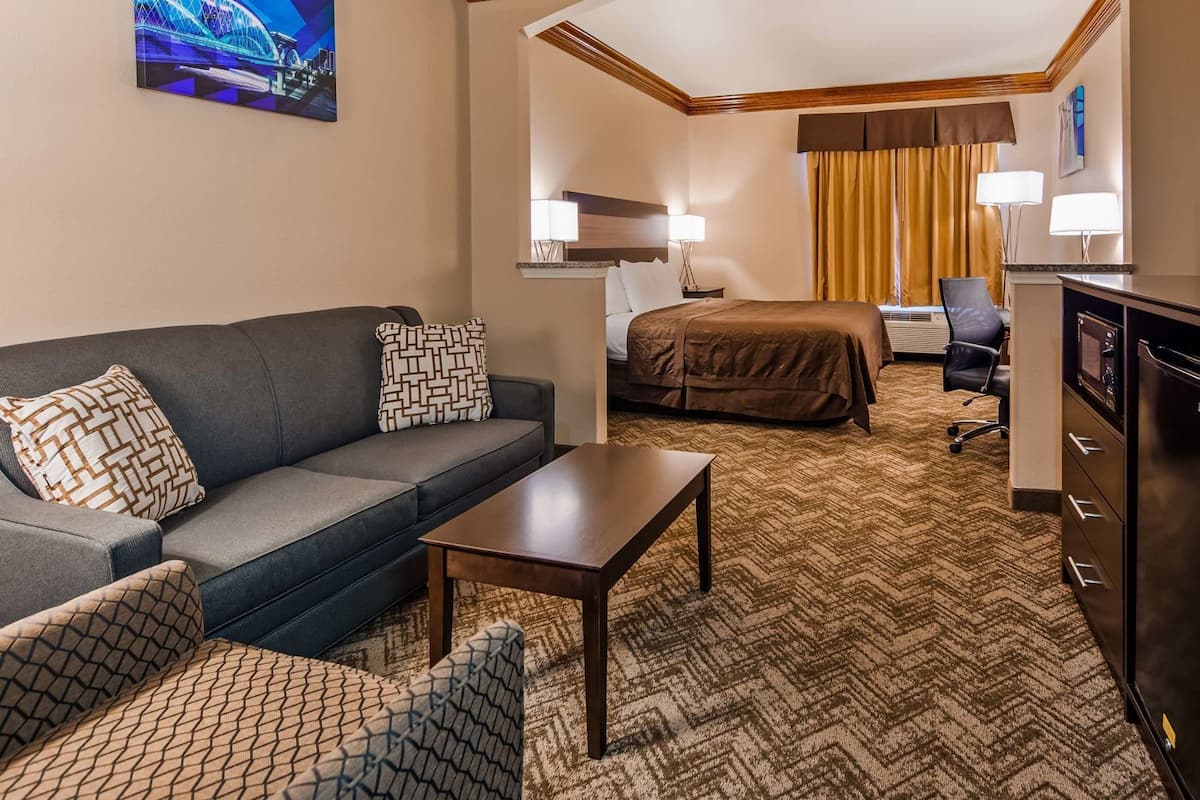 A hotel room with a sofa, a bed, a desk, a television, and a painting on the wall.
