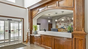 A reception area with a wooden reception desk, a glass door entrance, a plant, and a sign reading "FORT WORTH STOCK YARD". - Best Western Fort Worth Inn & Suites (Fort Worth)