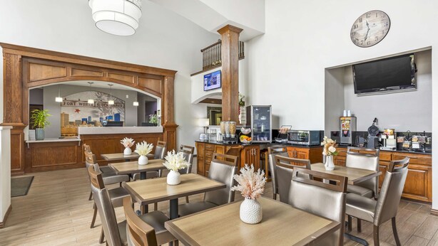 A spacious dining area with wooden tables and chairs, a kitchen area with modern appliances, and a large clock on the wall. - Best Western Fort Worth Inn & Suites (Fort Worth)