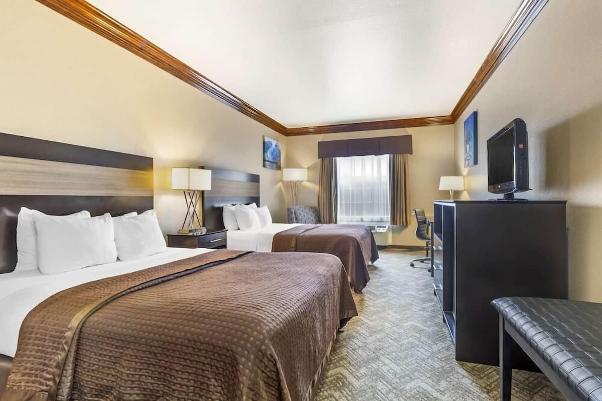A hotel room with two beds, a desk, a television, and a window with curtains.