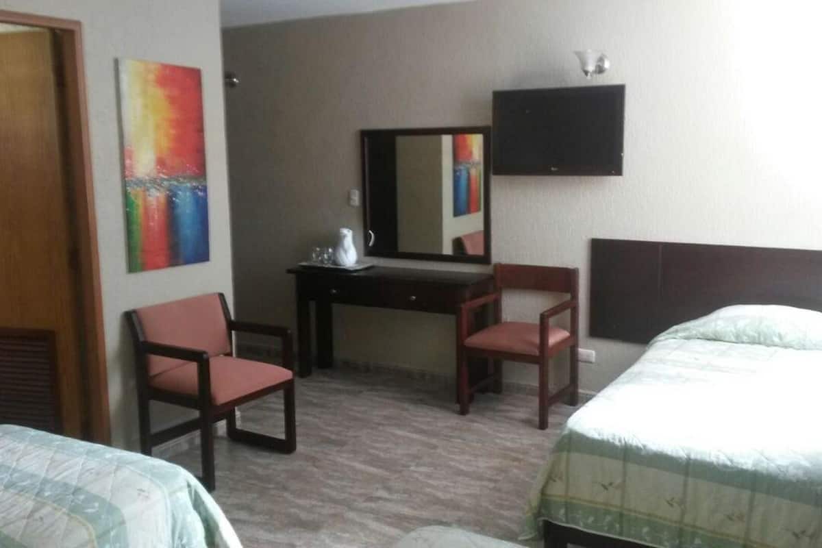 A hotel room with two beds, a desk with a chair, a mirror, and a television.