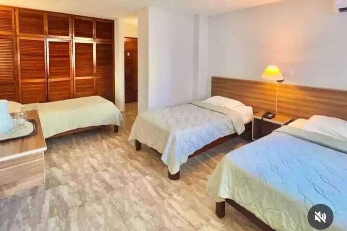 A hotel room with two single beds, a wooden wardrobe, and a nightstand with a lamp.