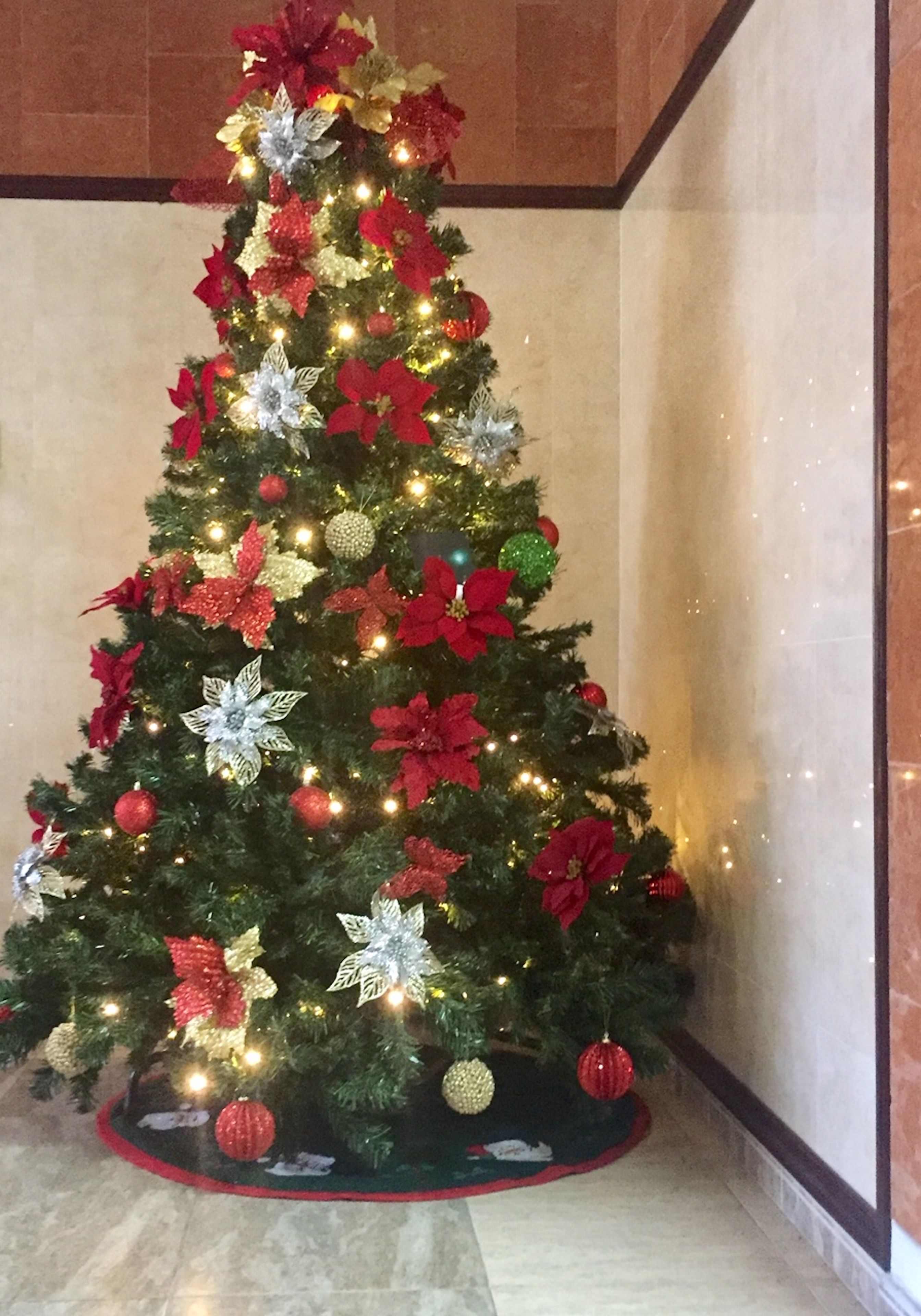 A Christmas tree decorated with red and silver ornaments, lights, and poinsettias.