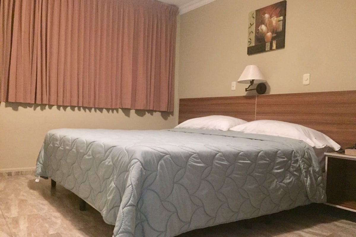 A hotel room with a bed, a nightstand, a lamp, and a painting on the wall.