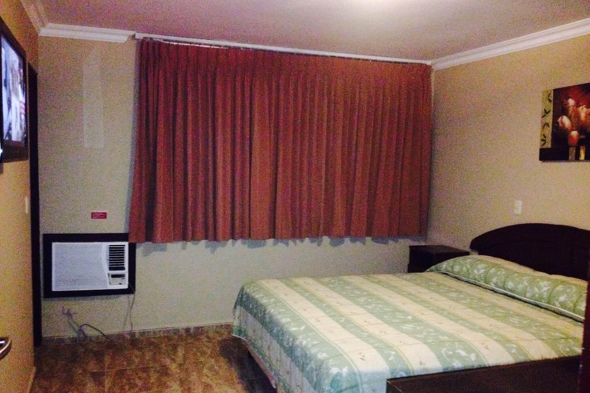 A bedroom with a bed, a television mounted on the wall, and a window with curtains.