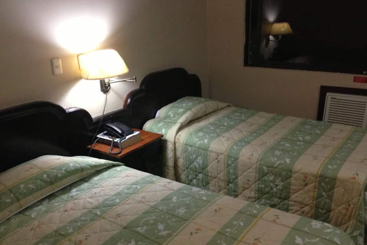 A hotel room with two beds, a nightstand with a phone, and a lamp.