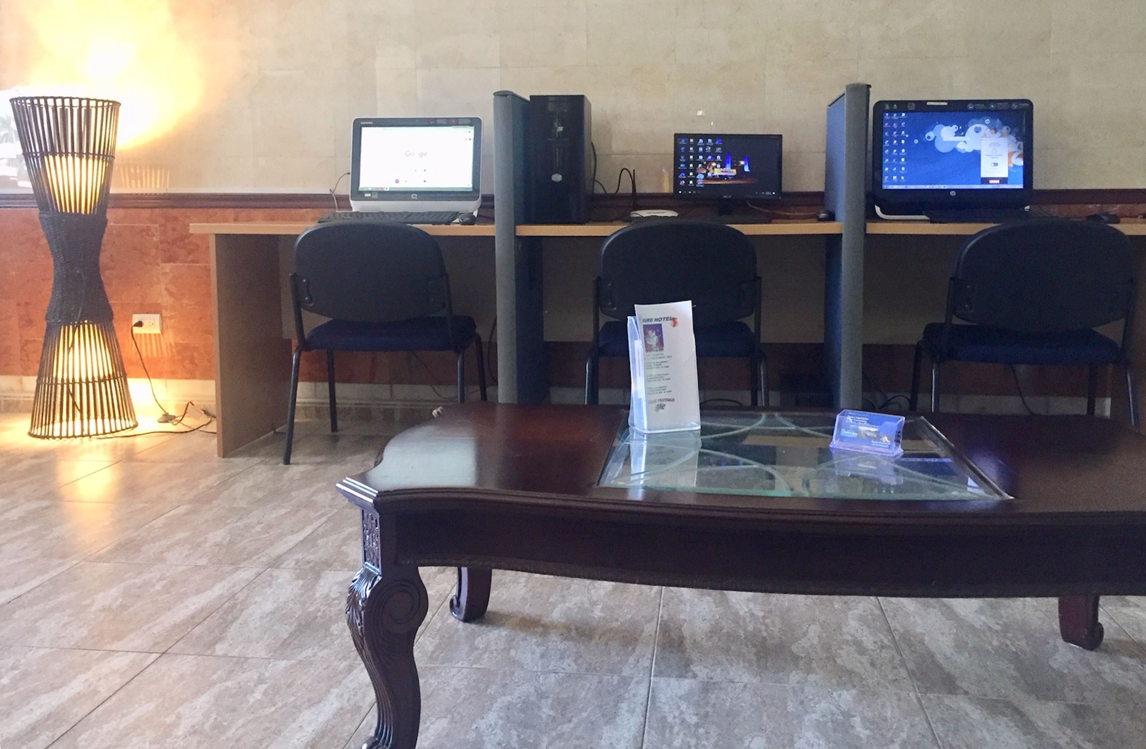 A reception area with a wooden reception desk, three black chairs, and two computer monitors displaying various applications.