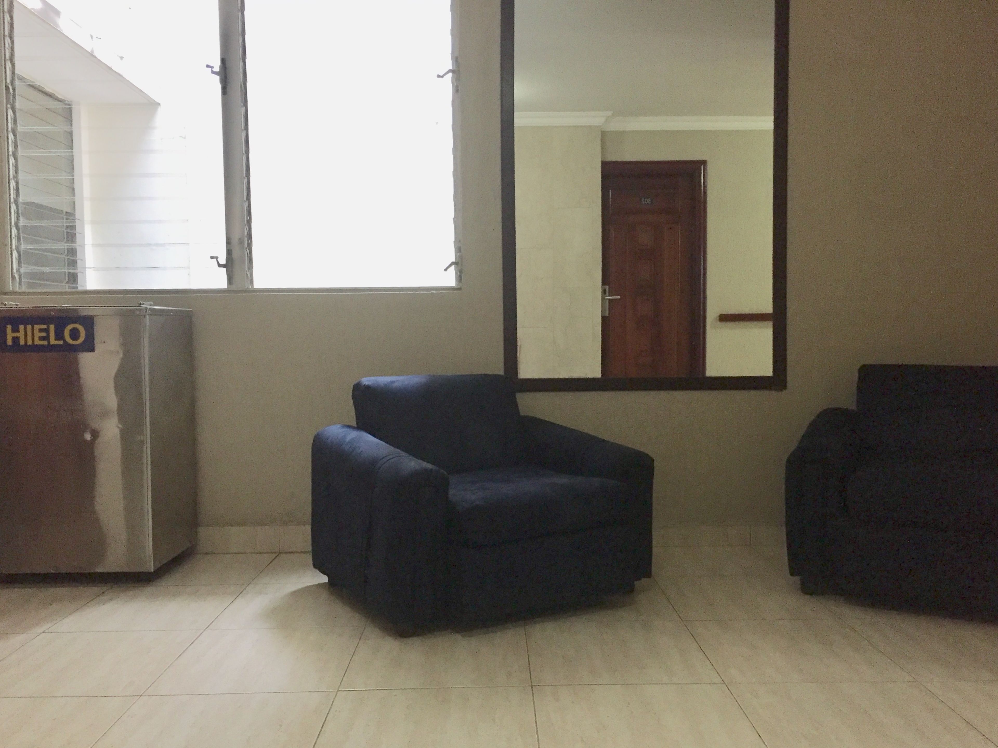 Una habitación con un espejo grande, dos sillones oscuros y un mueble metálico con la etiqueta 'HIELO'.