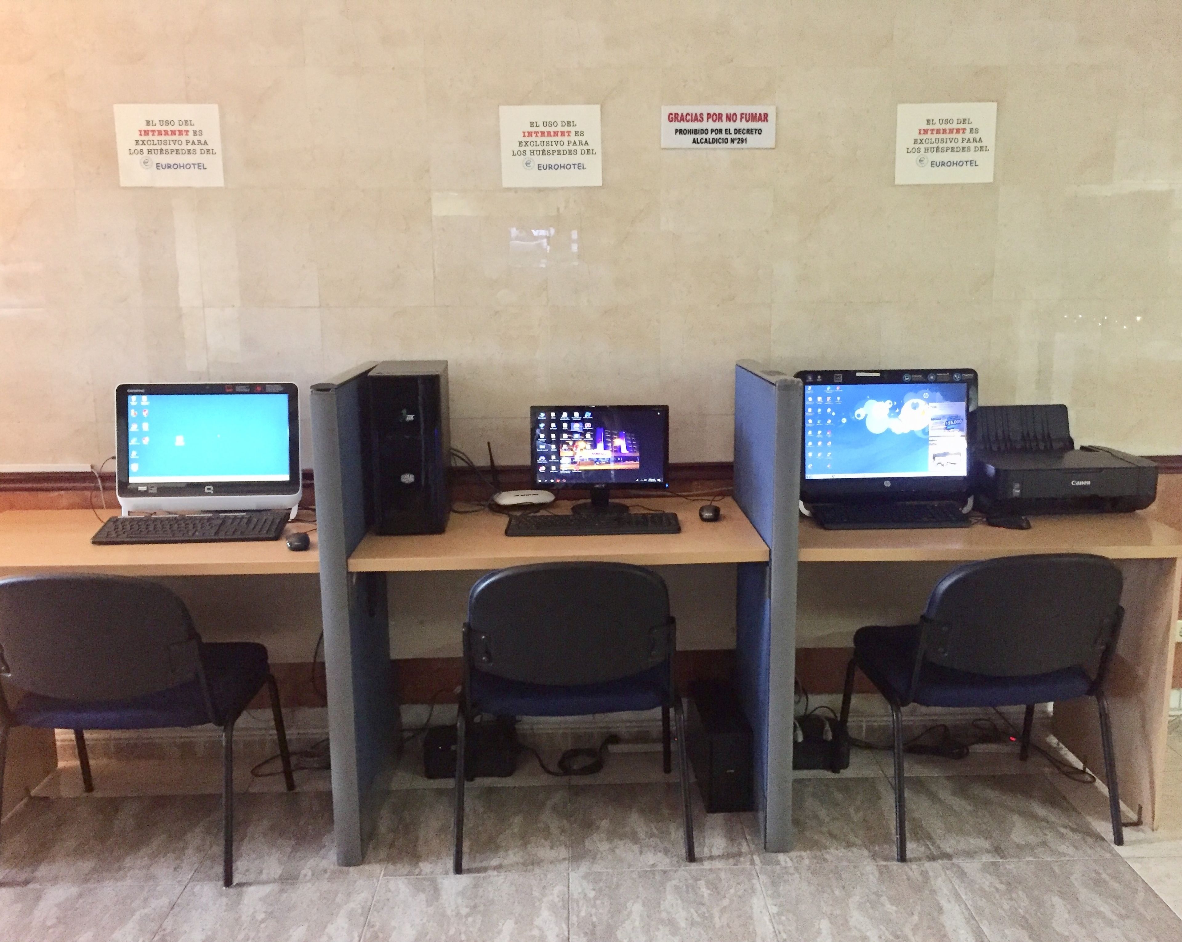A computer lab with three workstations, each with a monitor, keyboard, and mouse. There are signs on the wall indicating internet usage rules.