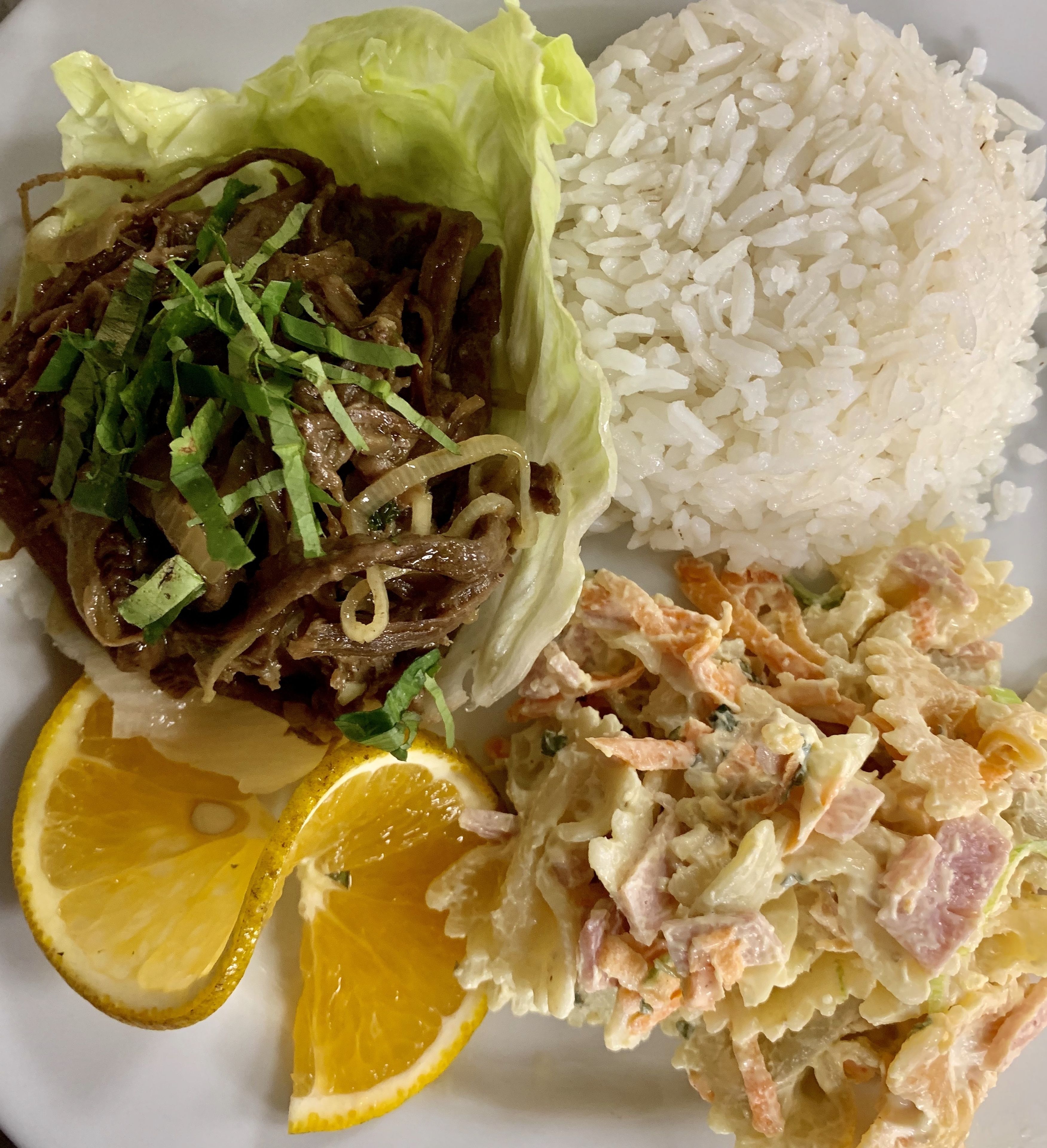 A plate with white rice, a beef dish with onions, a coleslaw, and a lemon wedge.