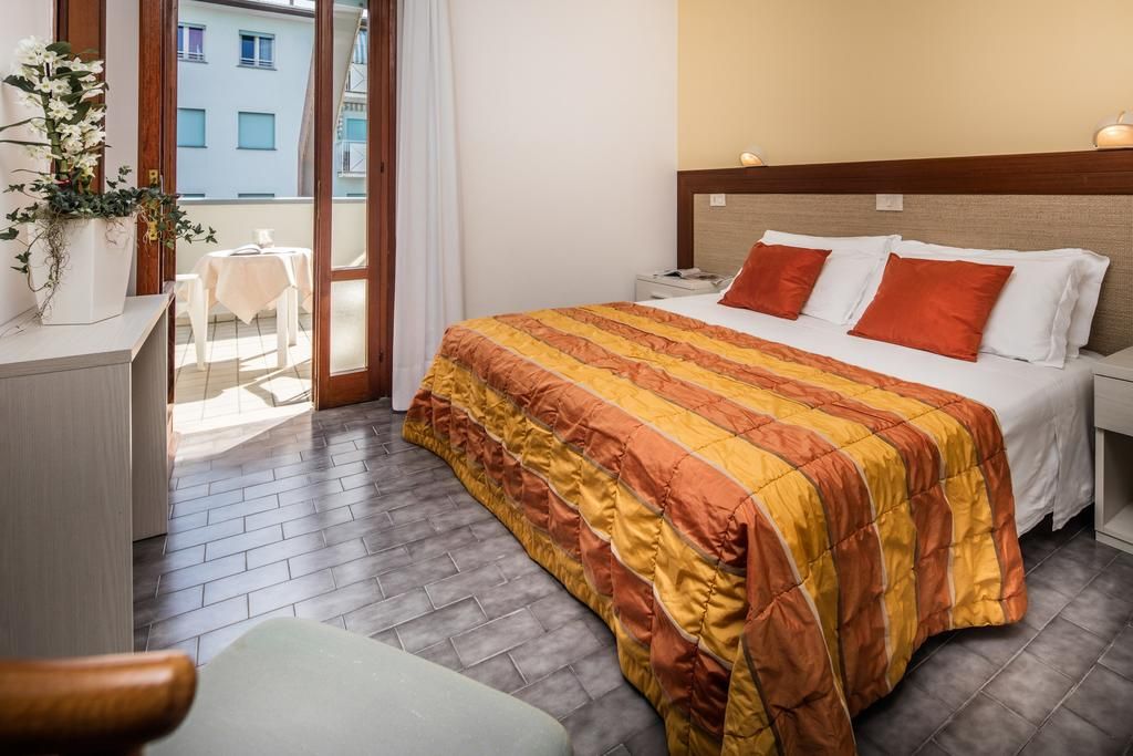 A hotel room with a bed, bedside table, and a view of the outside balcony.