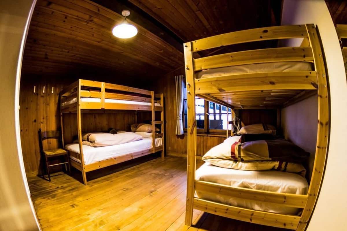A wooden cabin with bunk beds, a single chair, and a window with curtains.