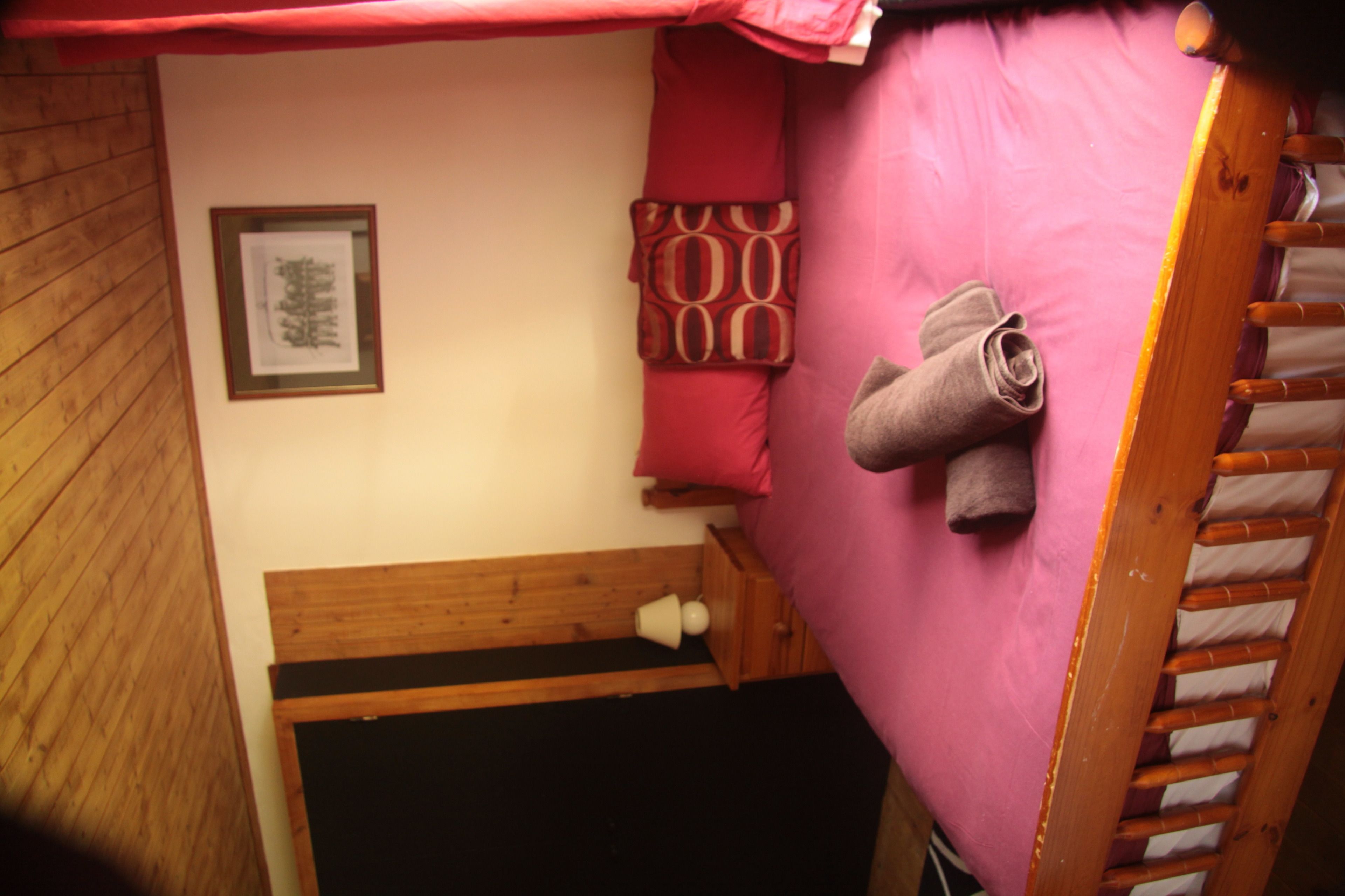 A small, cozy room with a wooden bench, a pink bed with a ladder, and a framed picture on the wall.