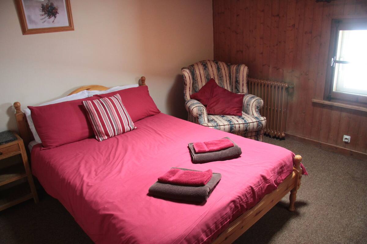 A bedroom with a large bed, a chair, a radiator, and a window.