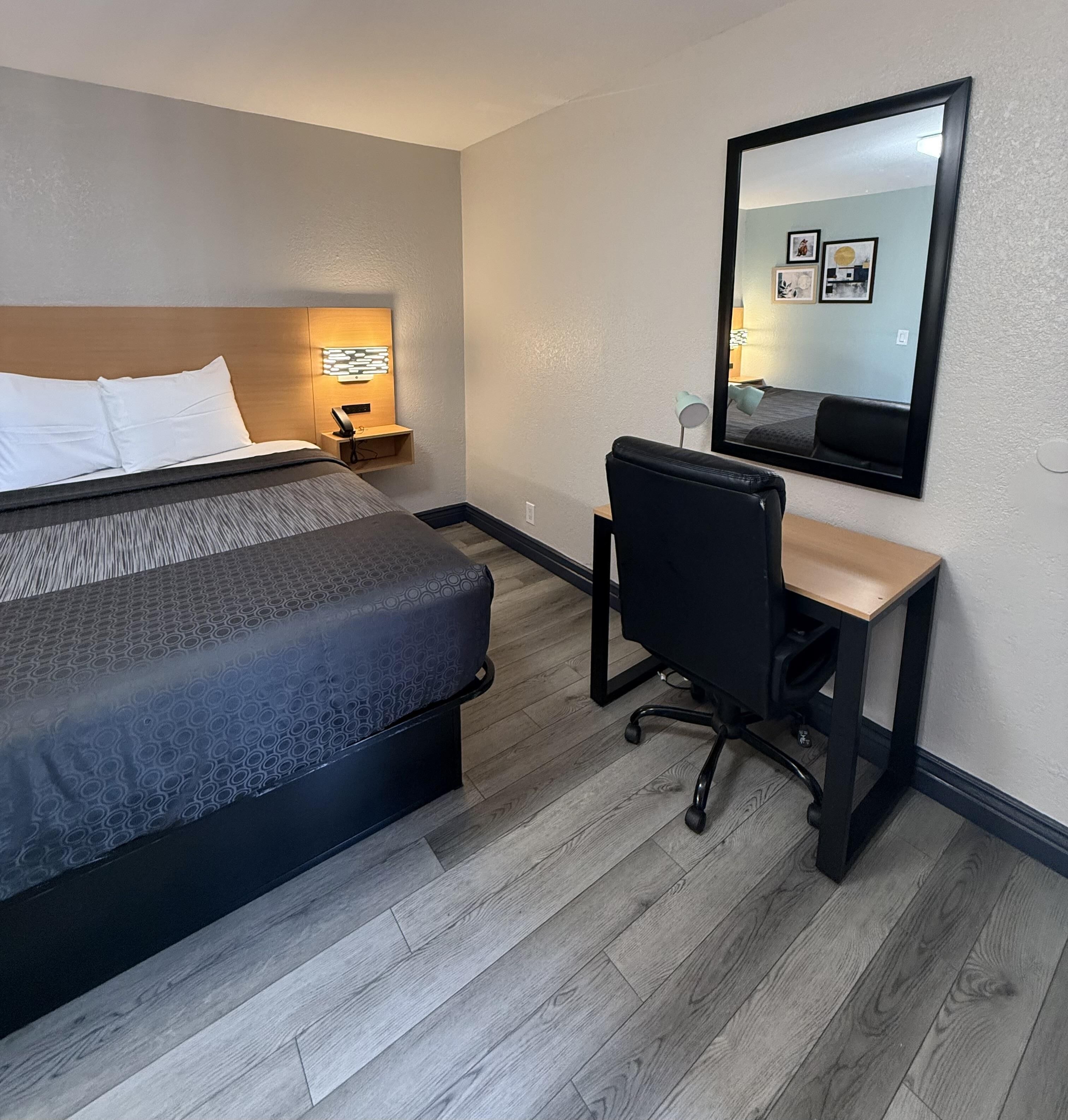 Una habitación de hotel con cama, escritorio, silla y un espejo grande.
