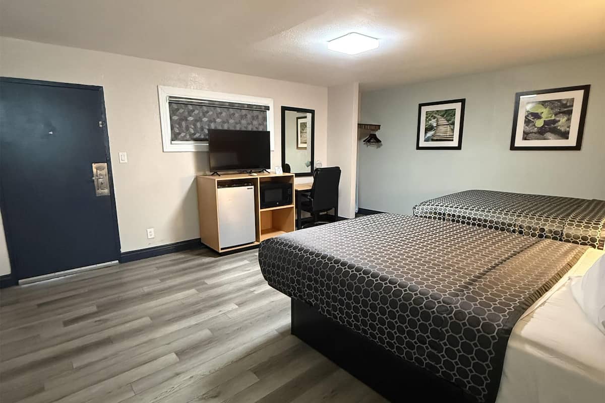 A hotel room with a bed, a desk with a computer, a television, and a door.