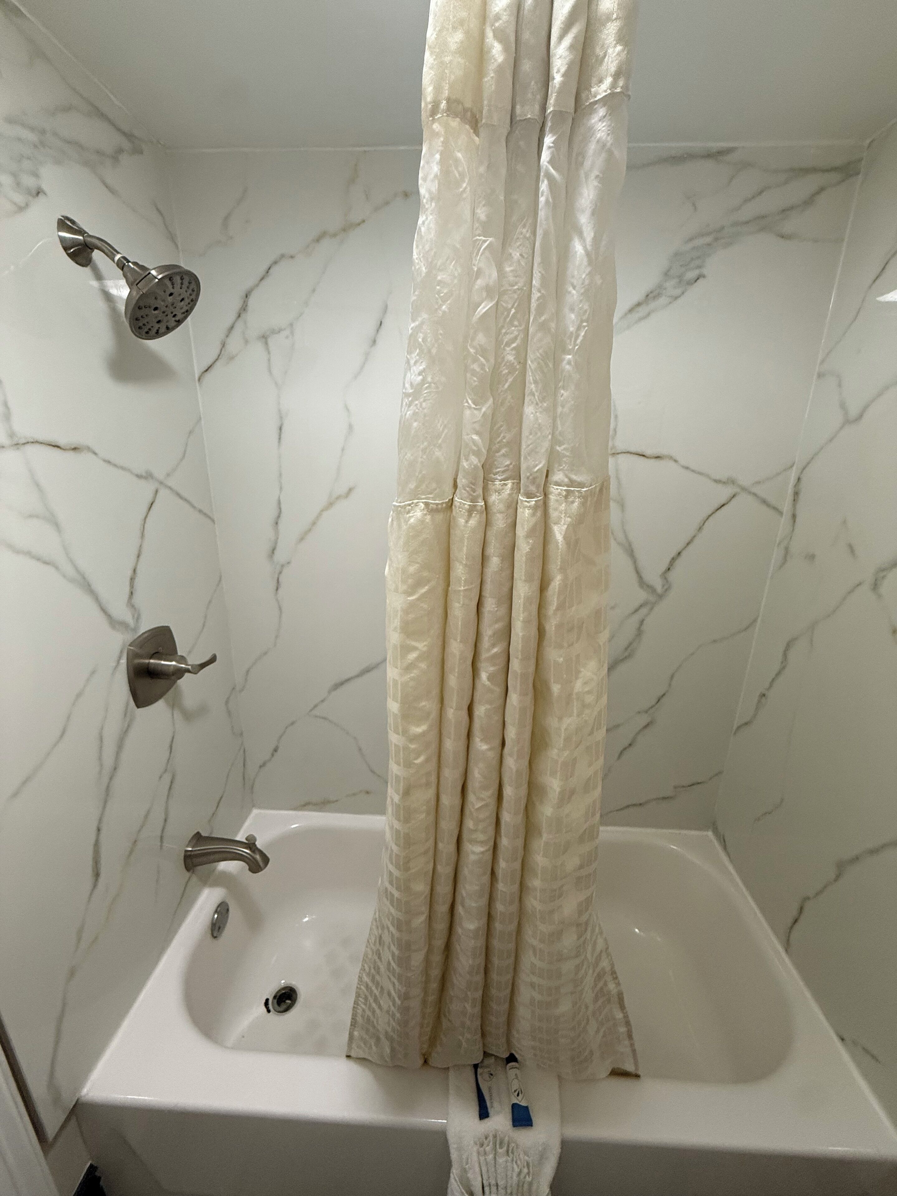 Un baño con pared de mármol blanco, una bañera blanca y un cabezal de ducha.