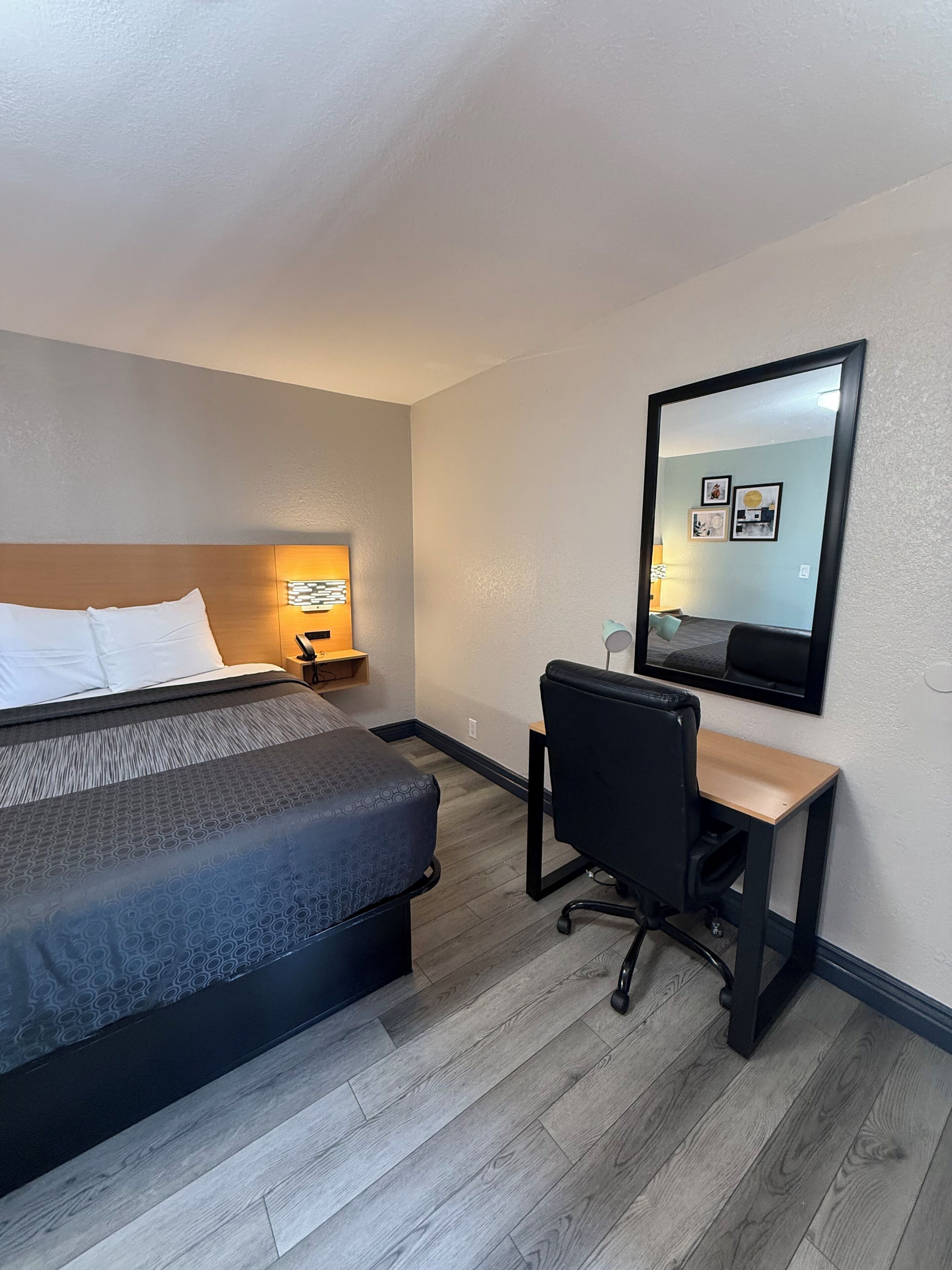 A hotel room with a bed, desk, chair, and a large mirror on the wall.