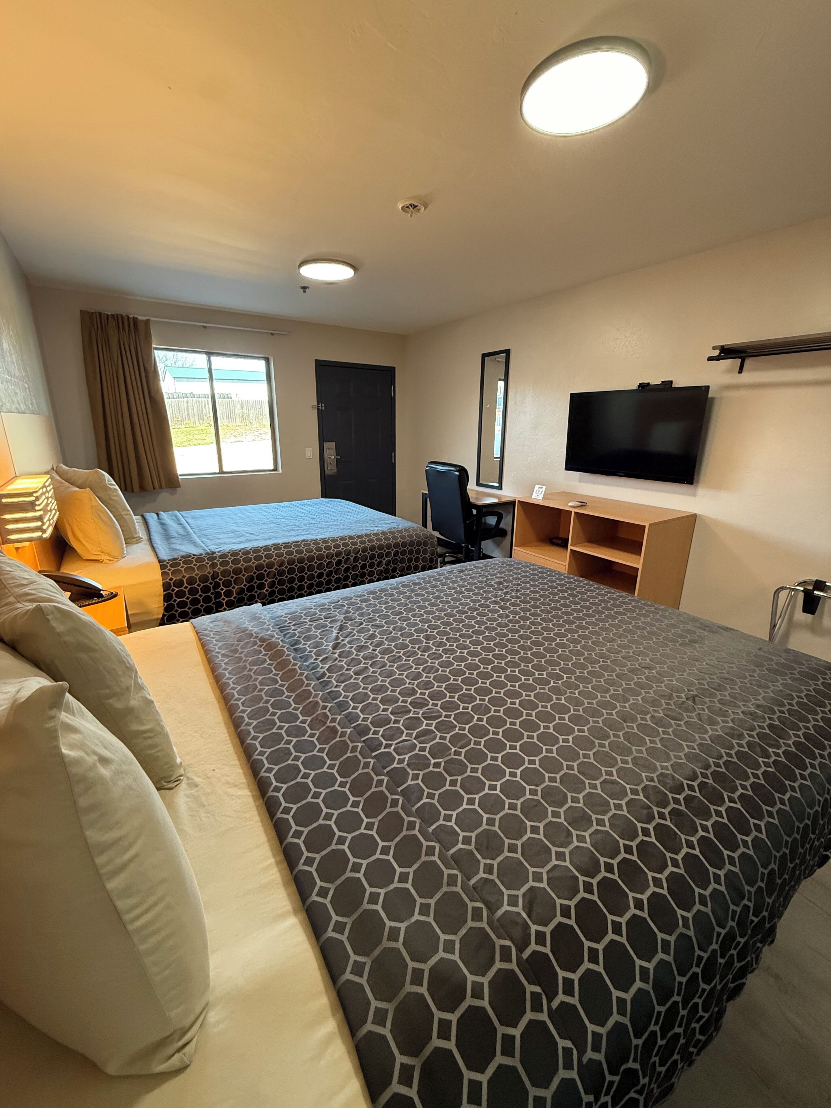 Habitación de hotel con dos camas, un escritorio, un televisor y una ventana con cortinas.