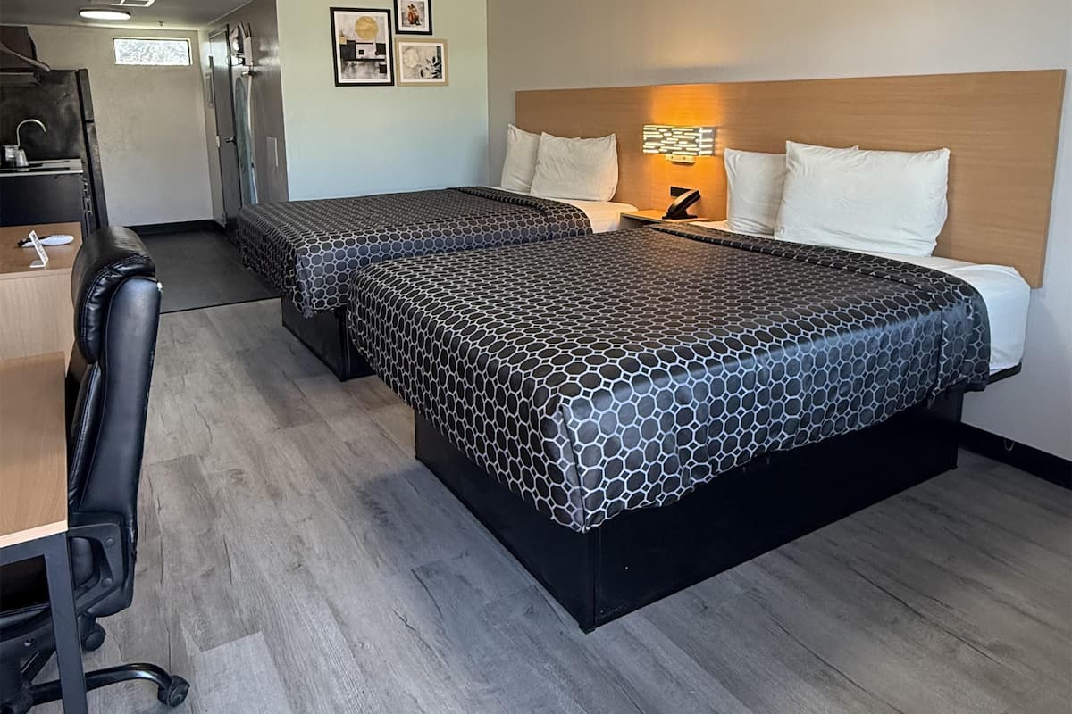 A hotel room with a bed, desk, chair, and a kitchenette.
