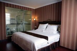 A hotel room with a large bed, a glass-enclosed shower, and a bedside telephone.