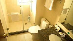 Un baño con cabina de ducha de vidrio, inodoro, lavamanos con encimera de granito y toallero con toallas.
