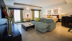 A modern hotel room with a sectional sofa, a flat-screen TV, a desk, and a bed with a headboard.
