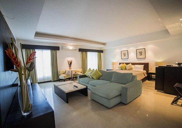 Una habitación de hotel moderna con sofá modular, televisión de pantalla plana, escritorio y cama con cabecera.