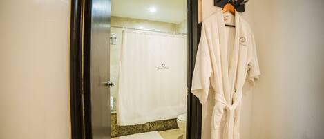 A bathroom with a shower curtain, a towel on the floor, and a robe hanging on a rack.