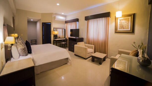 A hotel room with a bed, a desk, a chair, a TV, and a small table.