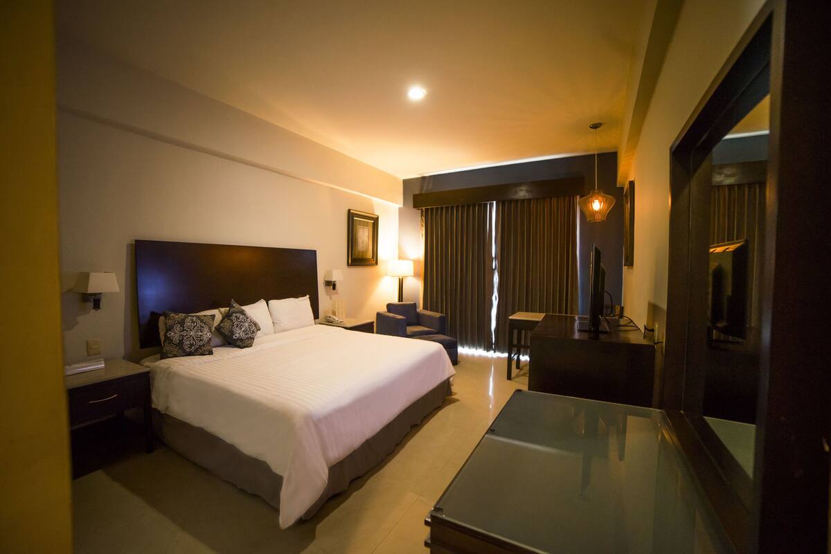 A hotel room with a large bed, a desk, a chair, a TV, and a mirror.