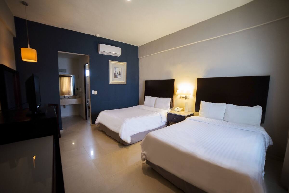 A hotel room with two beds, a desk, a chair, a mirror, and a picture on the wall.
