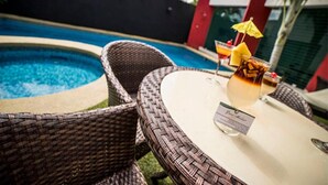 A poolside area with wicker chairs and a table, a drink with a straw, and a small umbrella.