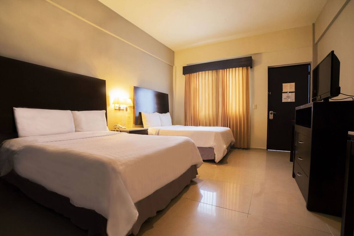 A hotel room with two beds, a desk, a TV, and a door.