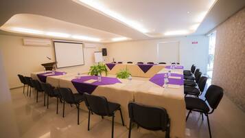 A conference room with a long table, chairs, a projector screen, and a whiteboard.