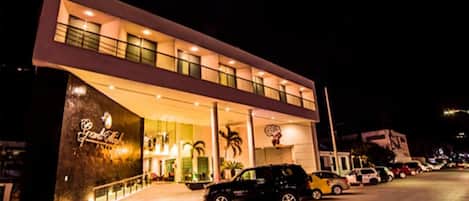 A modern hotel with a two-story facade, a prominent entrance with a glass canopy, and a parking area with several cars.