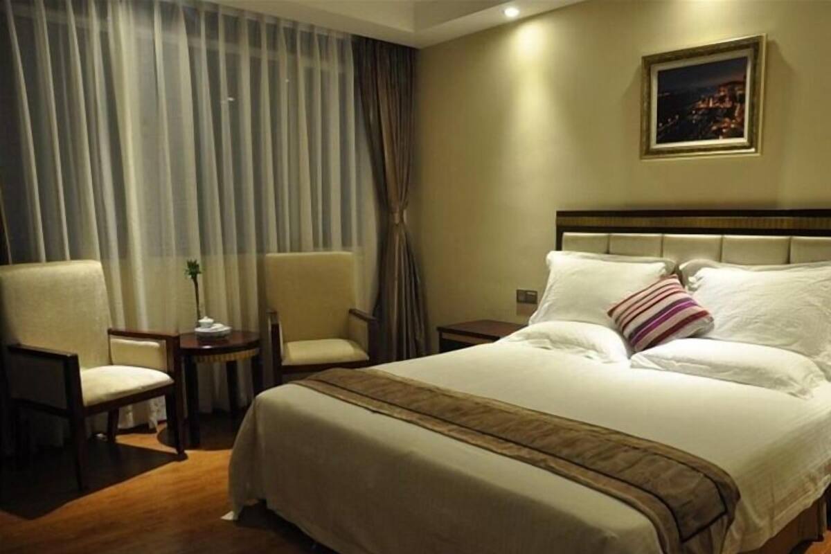Habitación de hotel con una cama grande, dos sillones, una mesita de noche y un cuadro en la pared.