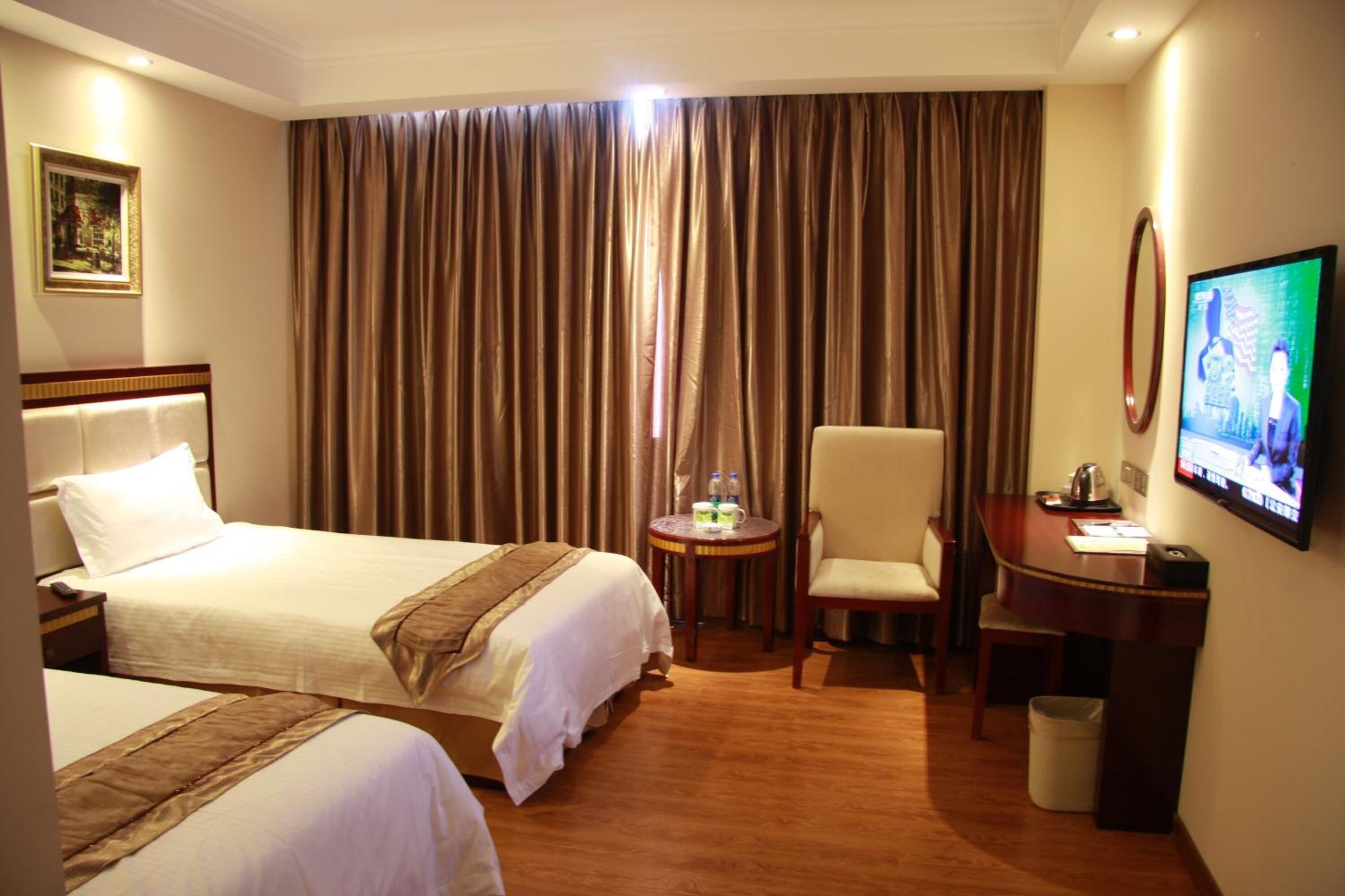 A hotel room with two beds, a desk, a chair, a television, and a window with curtains.