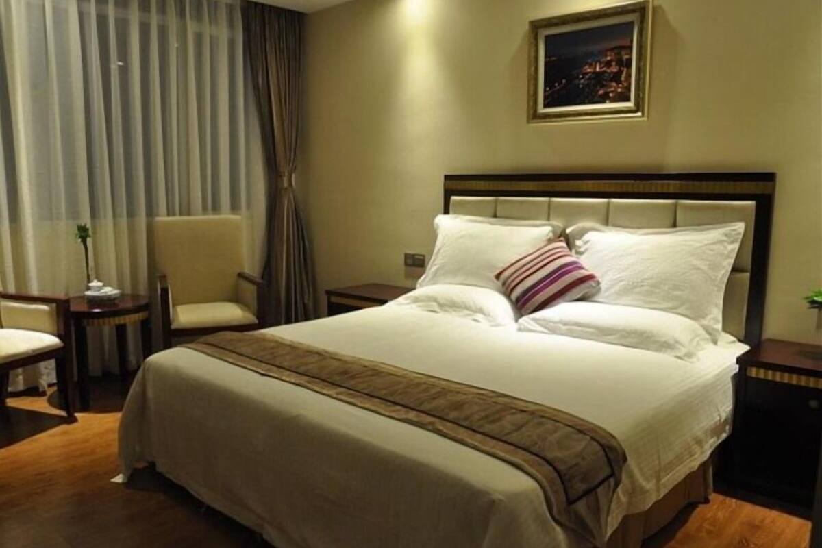 Habitación de hotel con una cama grande, una silla, una mesita de noche y un cuadro en la pared.