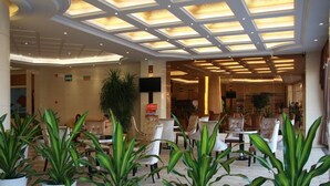 A hotel lobby with a modern design, featuring a central seating area with chairs and tables, surrounded by potted plants. - GreenTree Inn Shantou Chengjiang Road Business Hotel (Shantou)