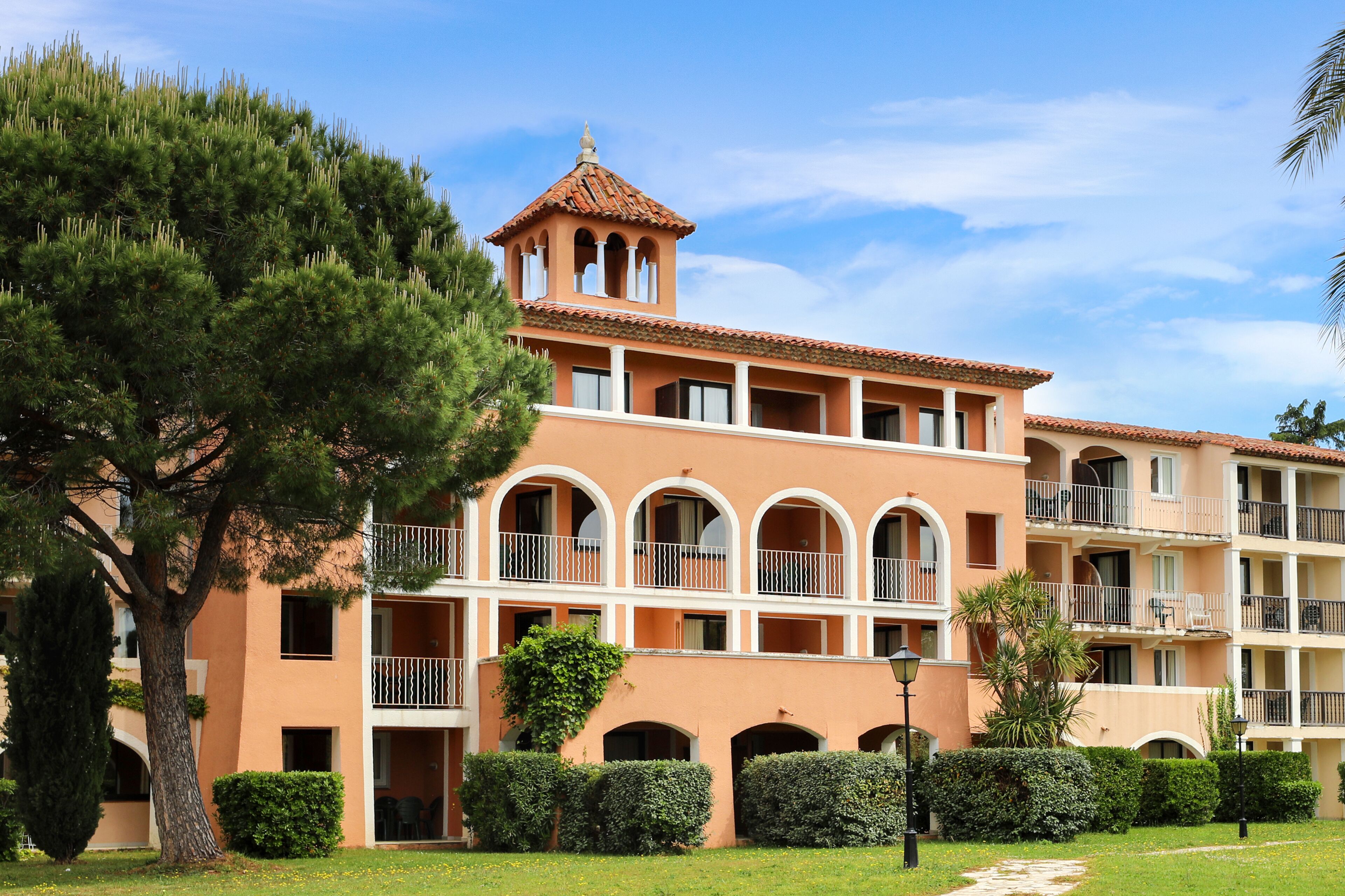 Un hôtel à plusieurs étages doté d’une tour centrale, de balcons et d’un jardin bien entretenu.