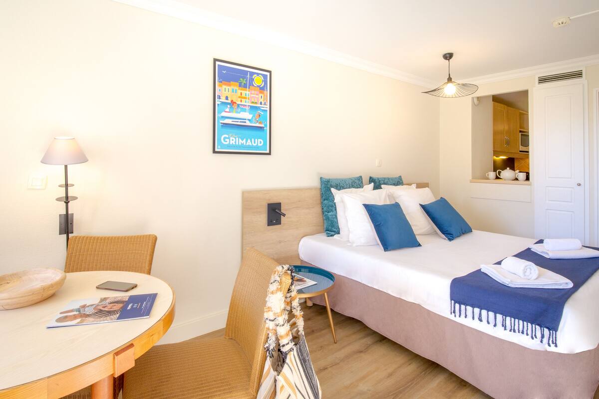 Ein Hotelzimmer mit einem Bett, einem kleinen Tisch mit Lampe, einem Sessel und einem gerahmten Bild an der Wand.