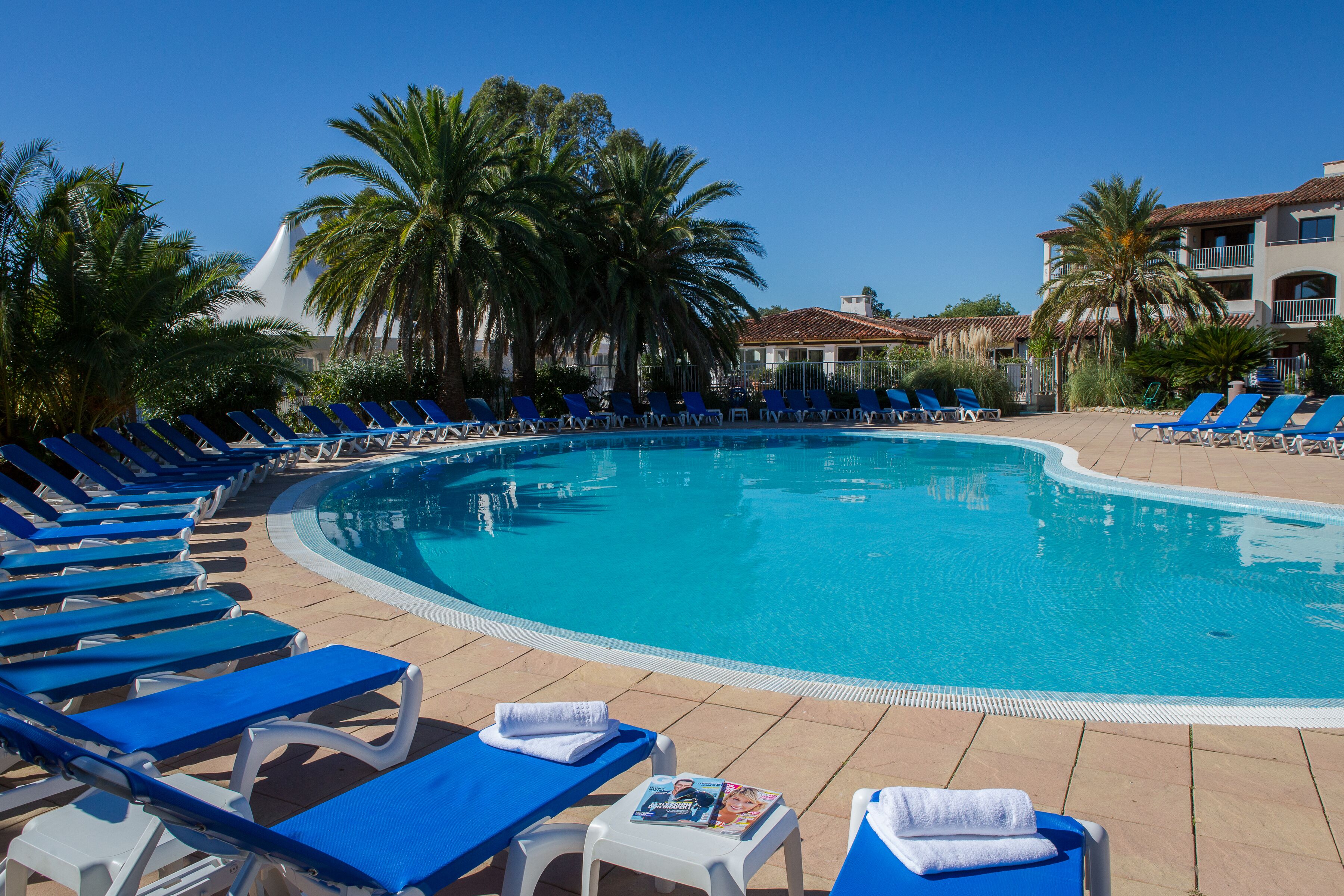 A pool area with blue lounge chairs and a white table with a magazine.
