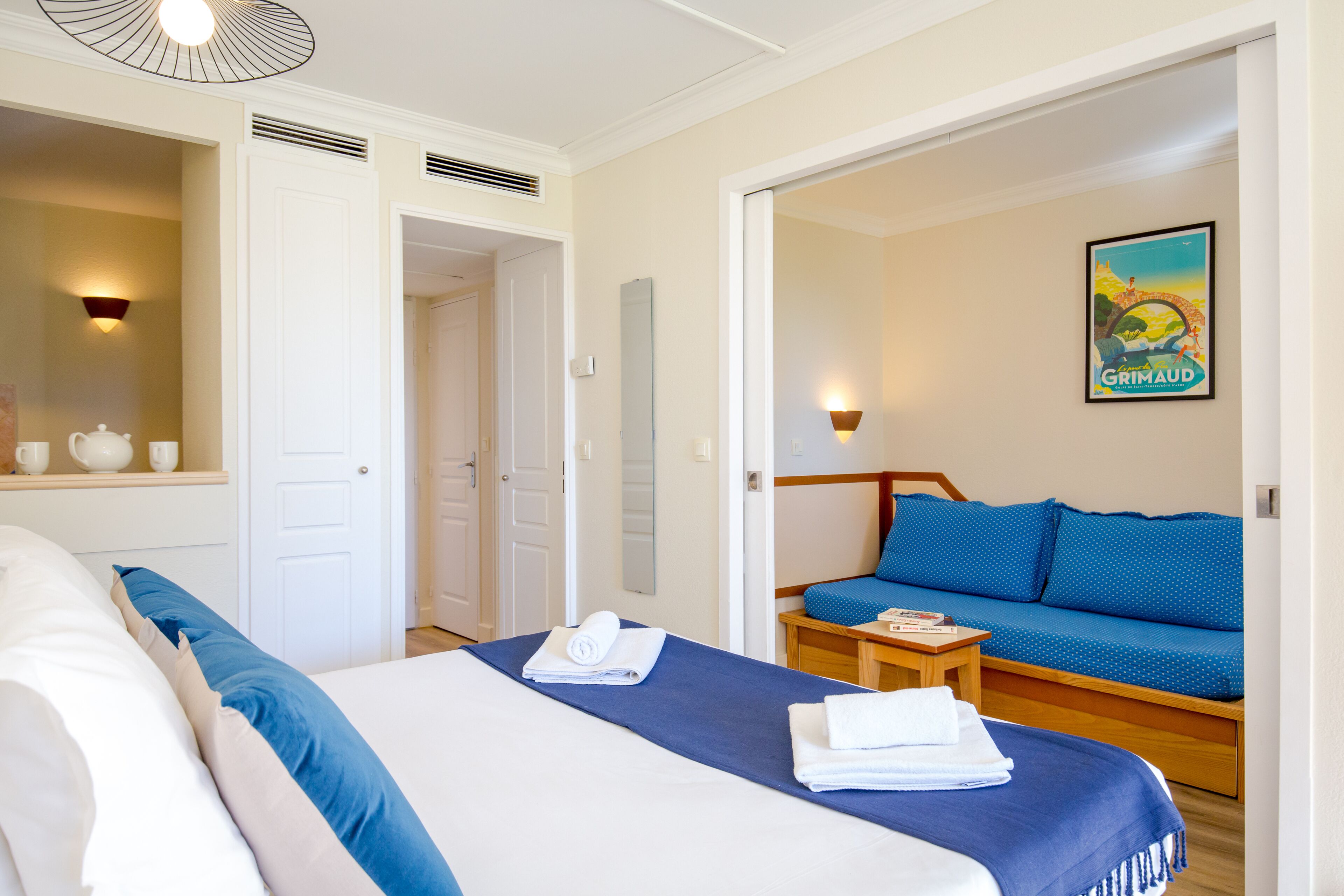 Une chambre d’hôtel avec un lit, un canapé, une petite table et un luminaire fixé au mur.