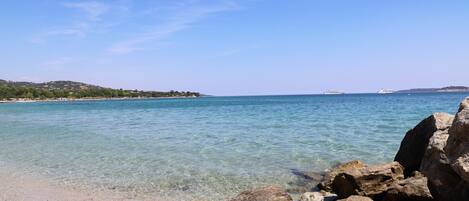 A beach with clear water, rocks, and distant hills.