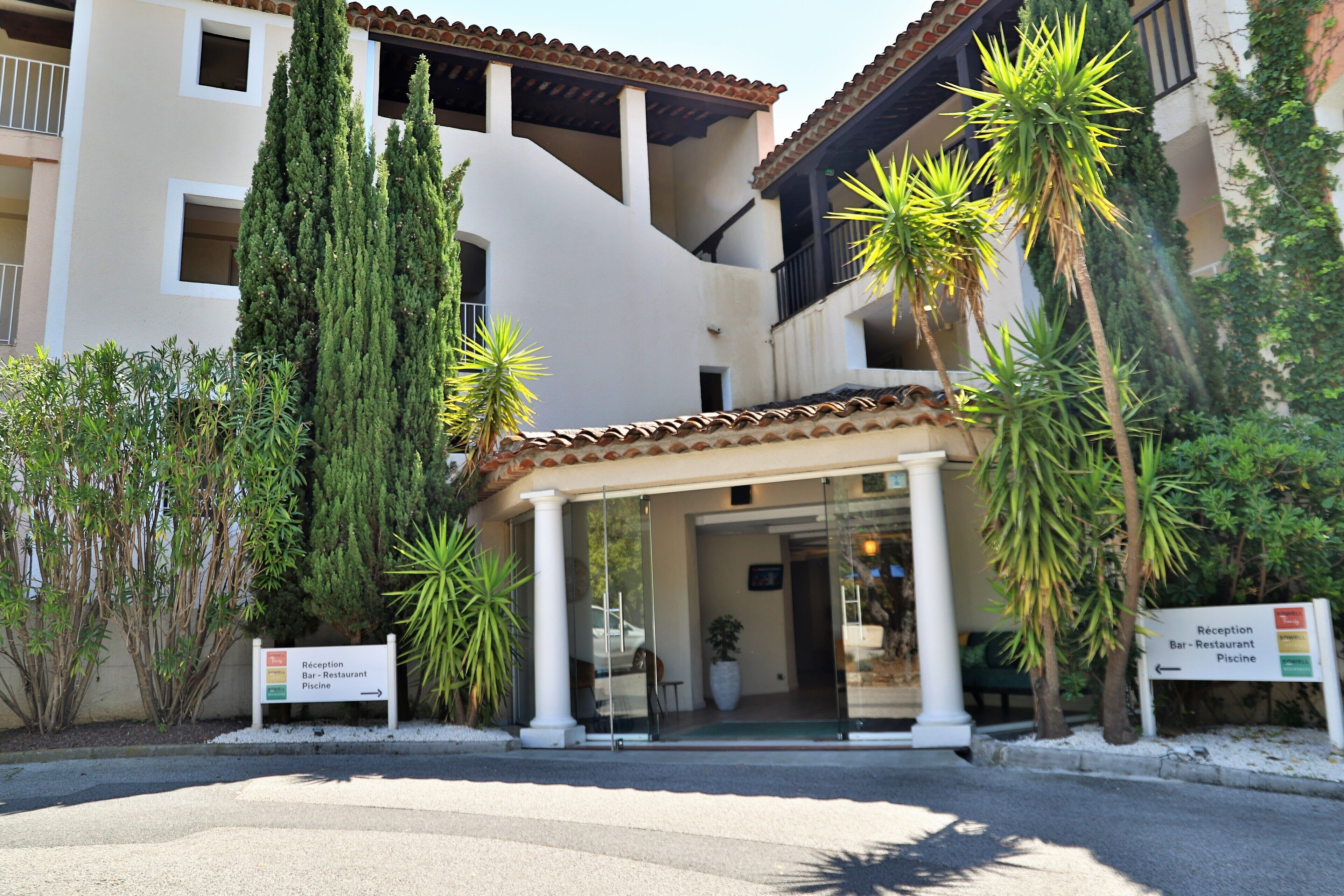 A hotel entrance with a reception desk, a bar/restaurant, and a pool area.