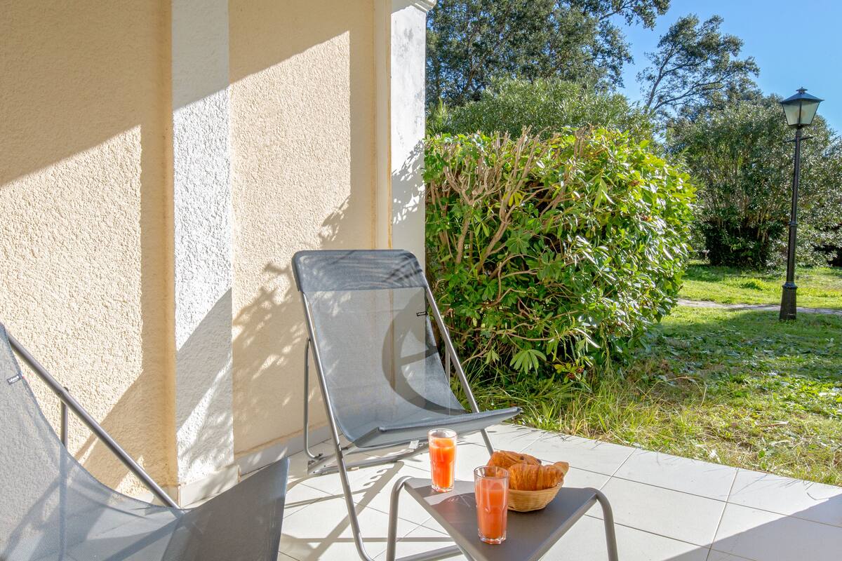 Eine Terrasse mit zwei Stühlen, einem Tisch mit Orangensaft und Croissants und Blick auf einen Garten mit einer Laterne.