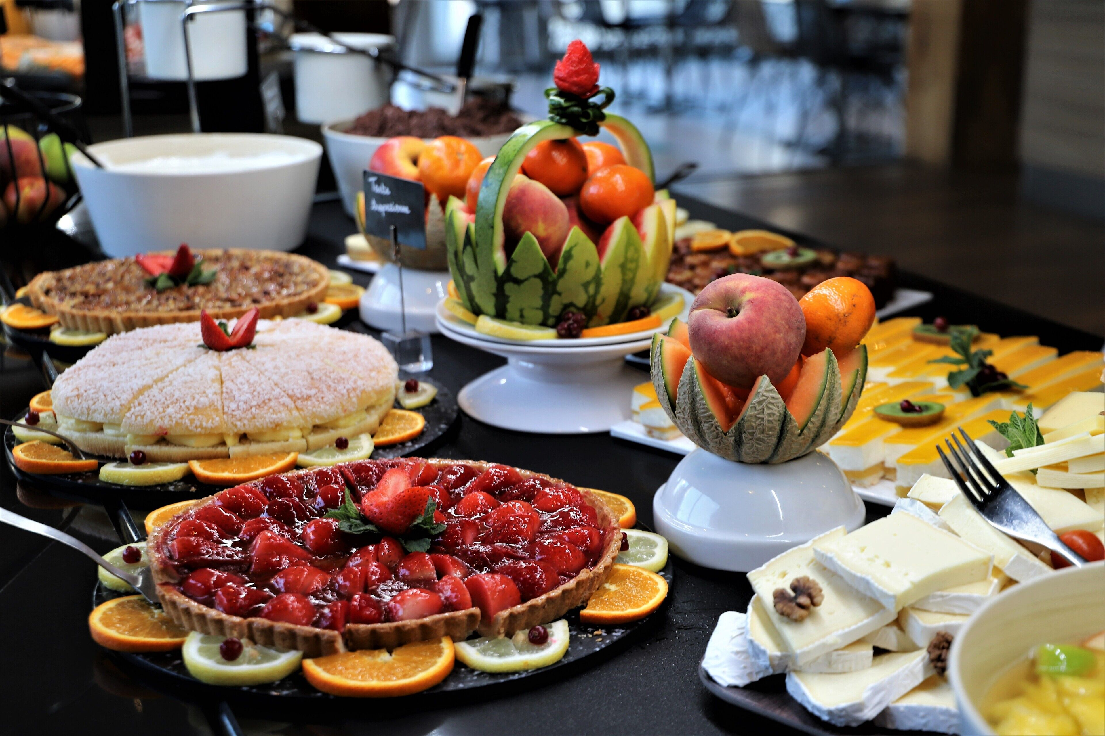 Un bufé con diversos alimentos, entre ellos tartas, frutas y quesos.